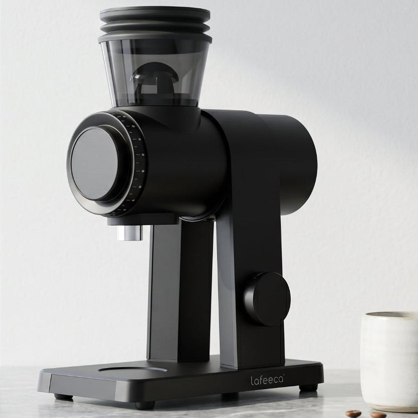 A black Lafeeca ARC coffee grinder with a clear bean hopper sits on a gray marble countertop next to a white ceramic mug and a glass jar of coffee beans in a bright, modern kitchen setting.